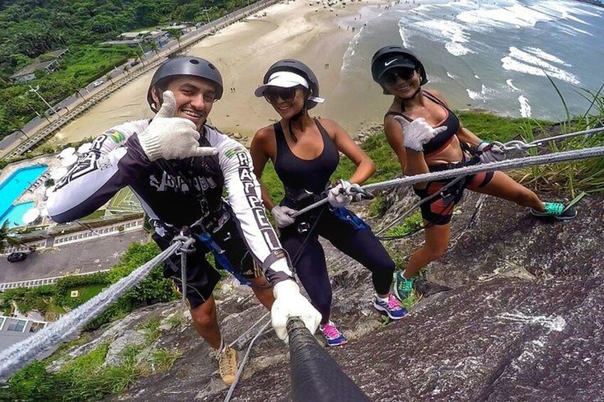 Three people rappelling down a cliff with a beach and ocean in the background. 3