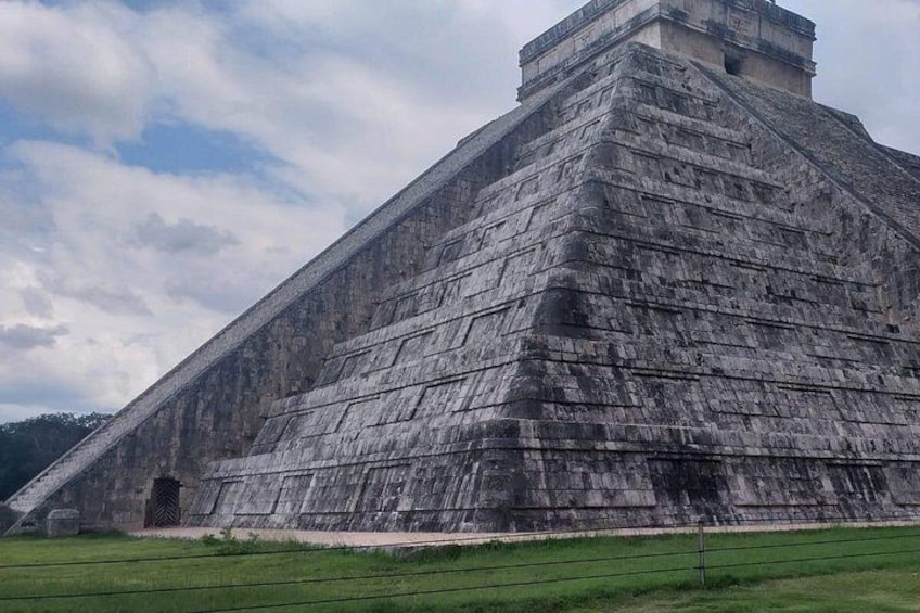 Eine große, pyramidenartige Struktur mit Stufenbau, umgeben von einem grünen Feld. 1