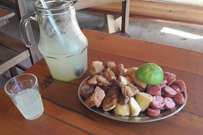 A plate of food with sausages and a lime, a glass of water, and a pitcher of a clear liquid on a wooden table. 4