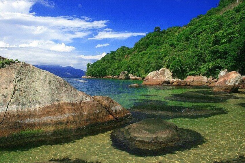 A coastal landscape with clear water, large rocks, and lush greenery. 4