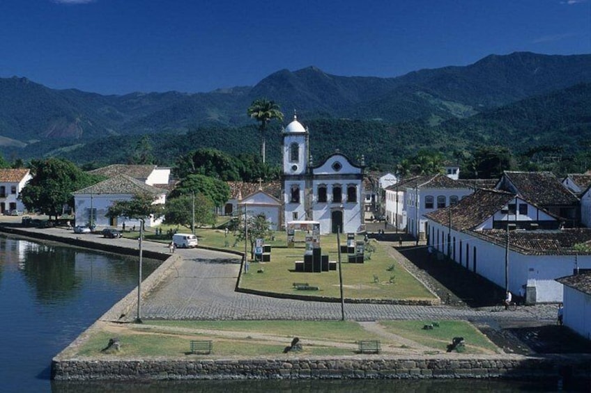 A coastal town with a prominent white church, a calm harbor, and lush green mountains in the background. 4