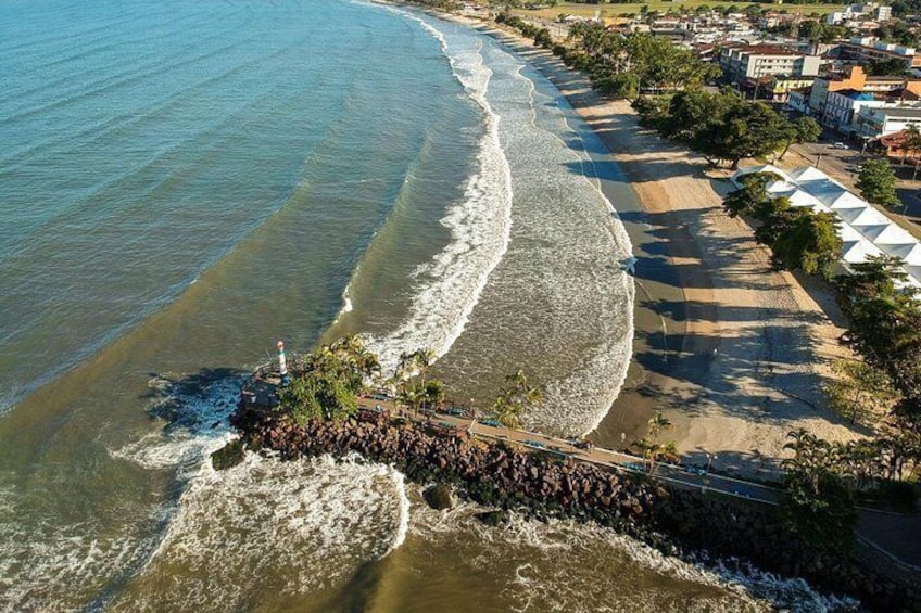 A coastal beach with waves, a lighthouse, and a paved walkway. 3