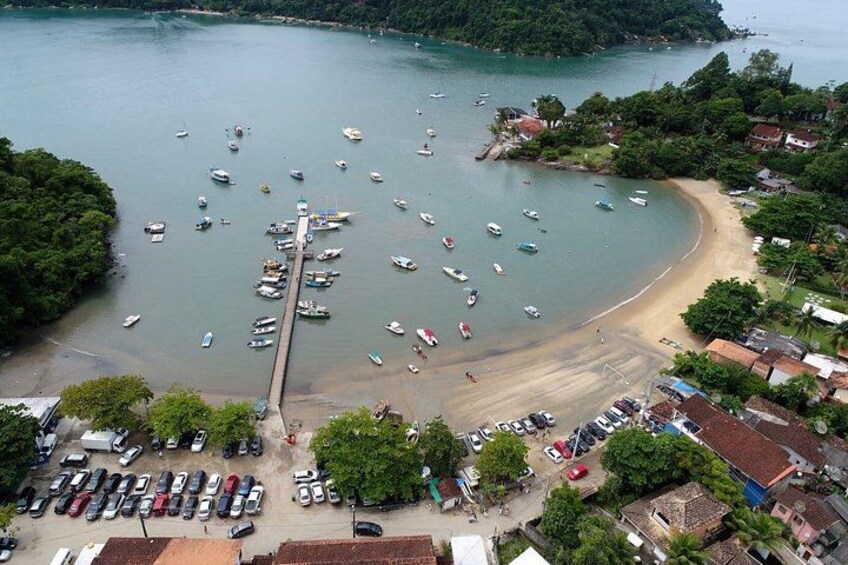 A coastal area with boats docked at a pier, a sandy beach, and a parking lot with cars. 2