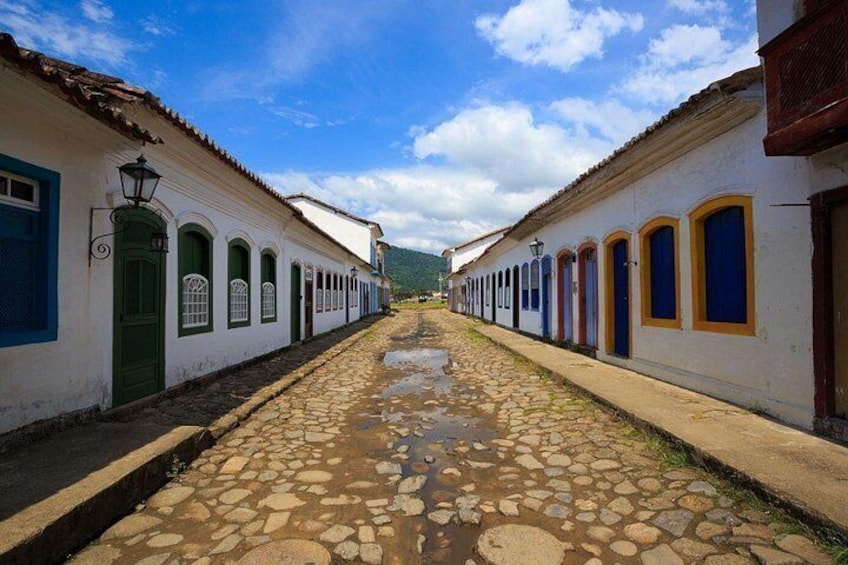A cobblestone street lined with white buildings with green doors and blue windows. 5