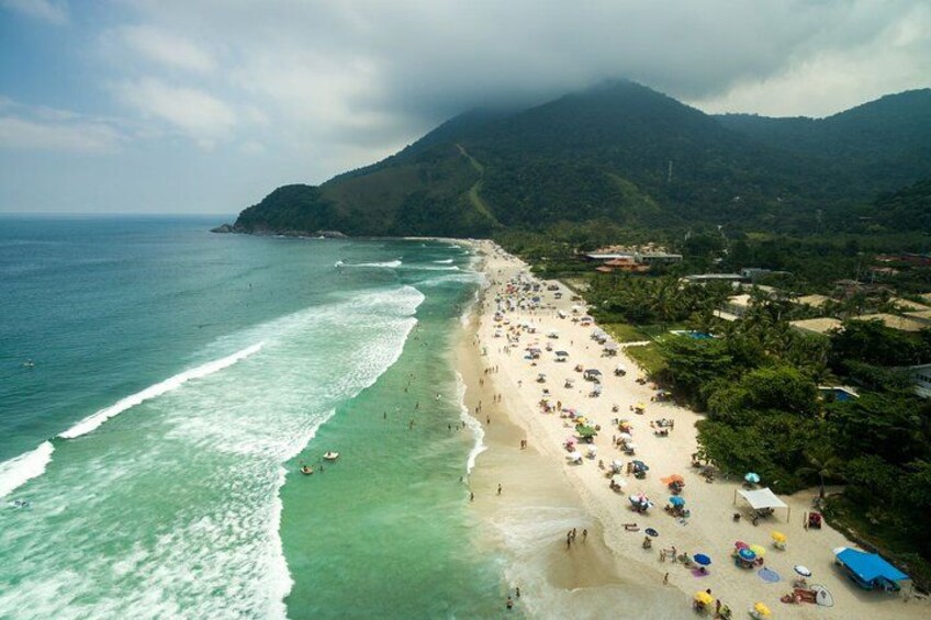 A beach with people, umbrellas, and a mountain in the background. 1
