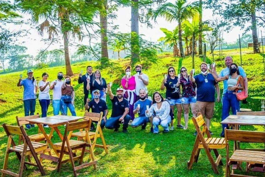 A group of people gathered outdoors with tables and chairs, surrounded by lush greenery and trees. 3