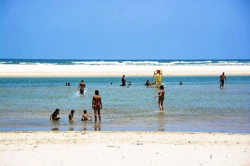 A beach with people swimming and standing in shallow water, a lifeguard tower, and a sandy shore. 4