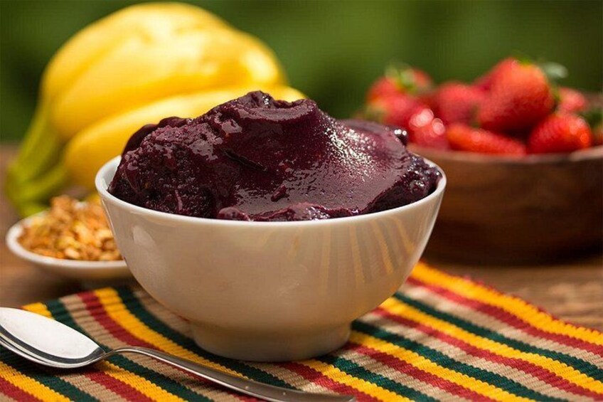 Un tazón de postre morado con una cuchara, rodeado de frutas y un paño colorido. 2