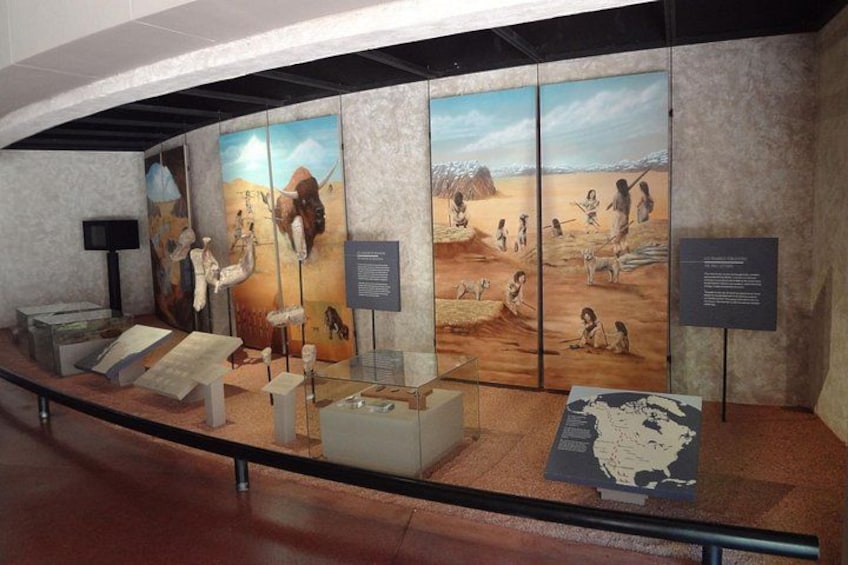 A museum exhibit with prehistoric artifacts and dioramas depicting early human life. 2