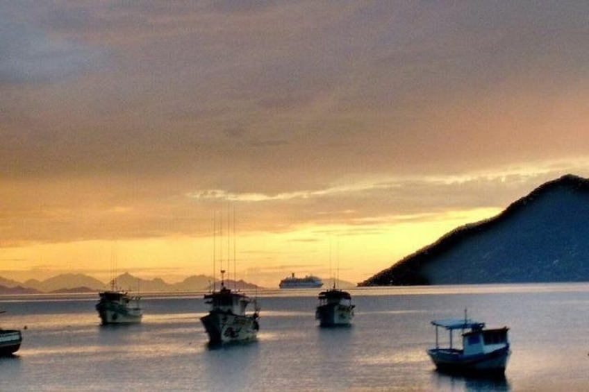 A calm sea with several boats, a distant ship, and a mountain in the background. 2