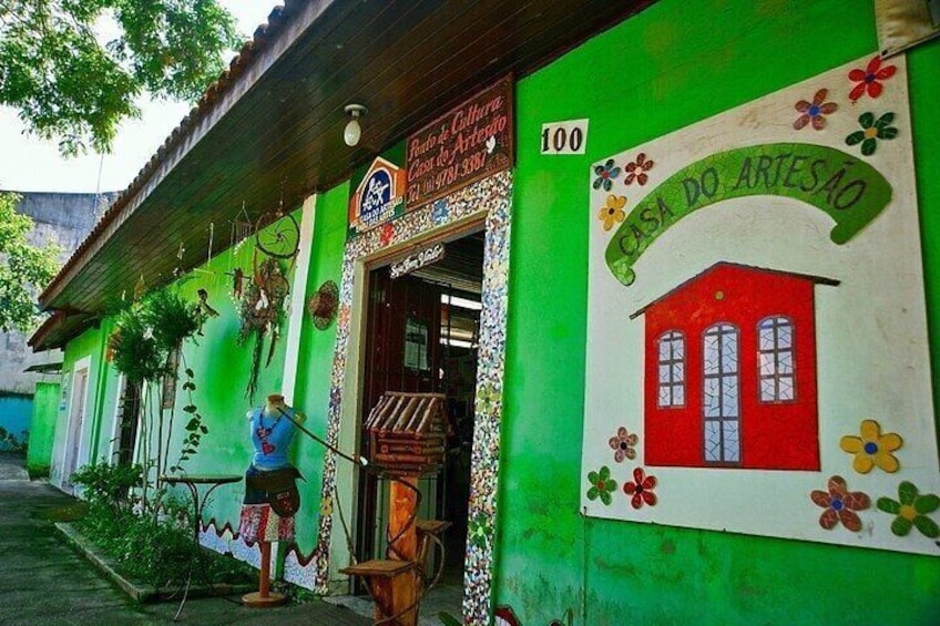 Een groen gebouw met een bord waarop 'Casa do Artesão' staat en een rode illustratie van een huis. 1