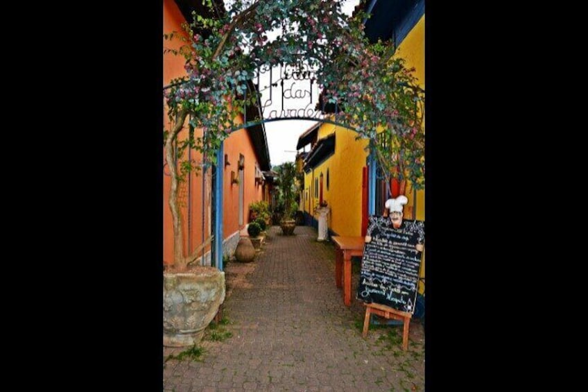 A narrow alleyway with colorful buildings, a stone planter, and a chalkboard sign. 2