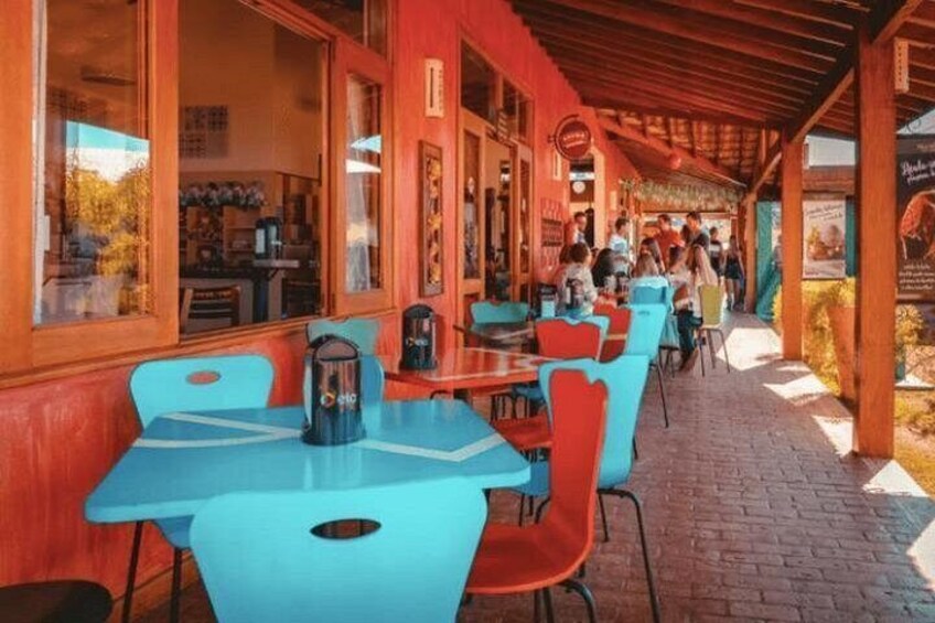 An outdoor cafe with red and blue tables and chairs, a brick floor, and a covered walkway. 4