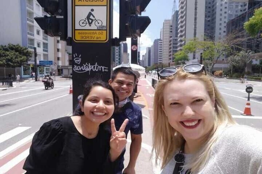 Three people posing in front of a traffic light with a bicycle symbol and a sign that says "No Vehicles." 5