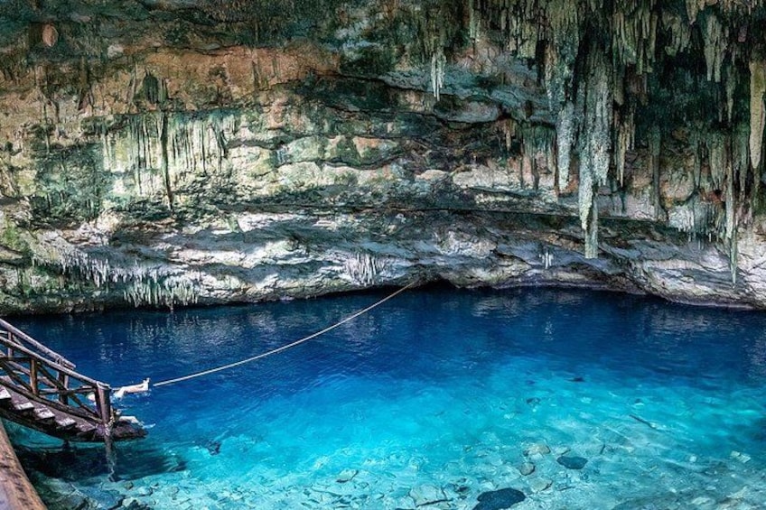 A clear blue pool with a wooden bridge, surrounded by rocky cliffs and stalactites. 2