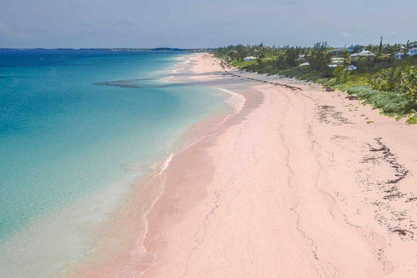 A beach with clear turquoise water, a sandy shore, and vegetation along the coastline. 1