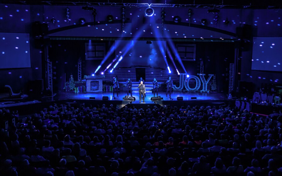 A stage with a large illuminated sign reading 'JOY' and a crowd of people seated in an auditorium. 4