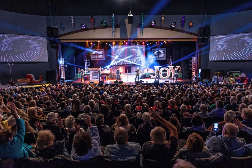 A concert with a large audience, stage lighting, and a band performing. 3