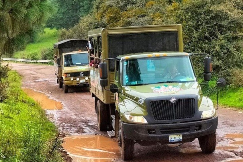A convoy of military vehicles driving on a muddy road surrounded by greenery. 3