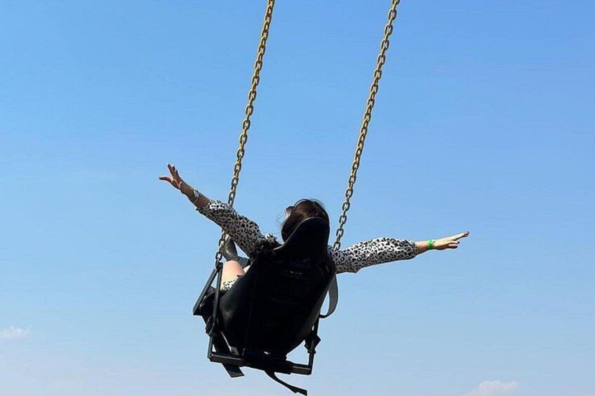 A person on a swing with outstretched arms against a clear sky. 5
