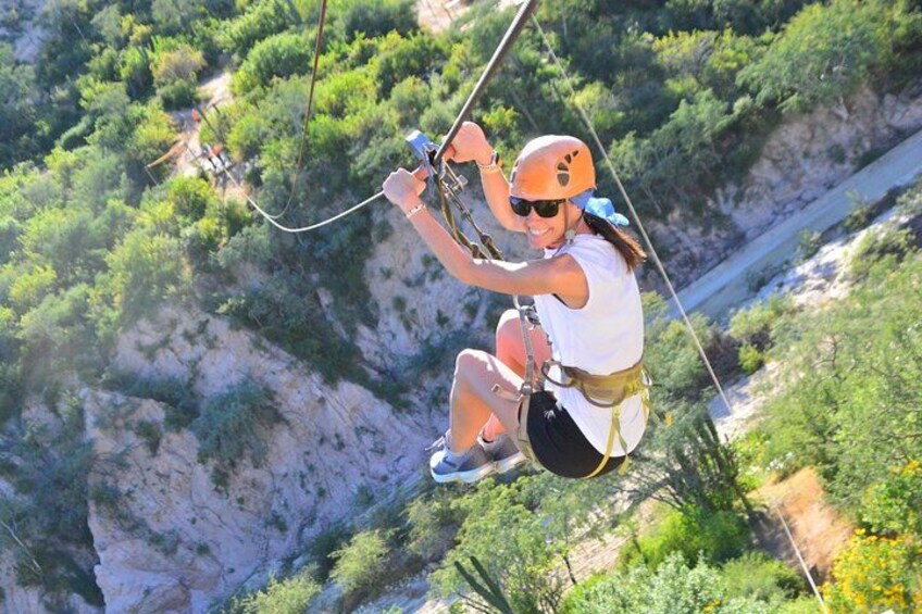 A person bungee jumping from a cliff with a harness and helmet, surrounded by greenery and rocky terrain. 2