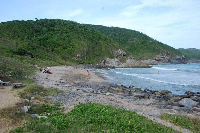 A beach with rocky terrain, people sunbathing, and a green hillside in the background. 3