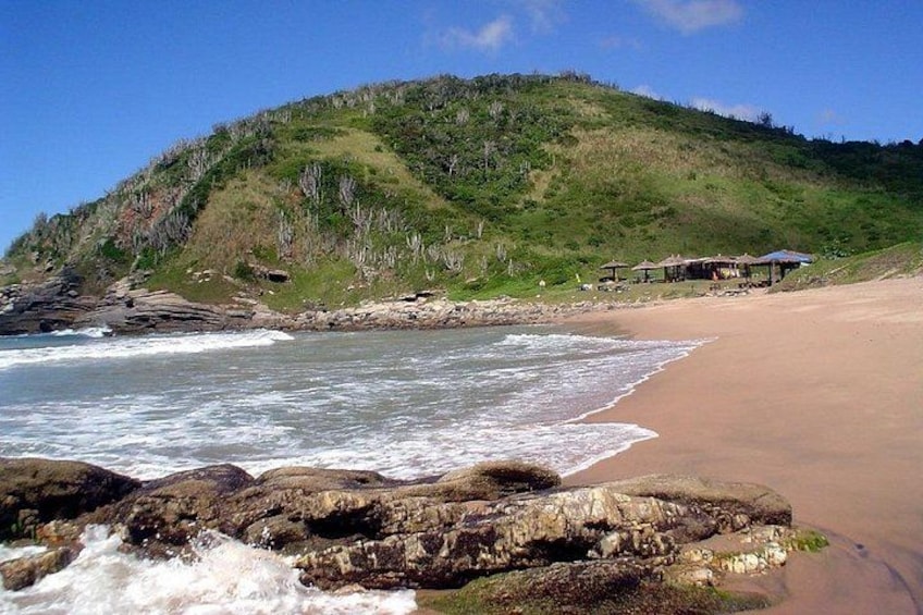 A beach with waves, a rocky shoreline, and a hill with buildings. 1