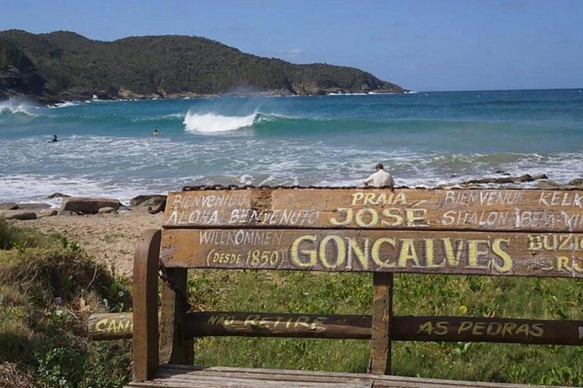 A beach with waves, a wooden sign with names, and a person sitting on a bench. 2