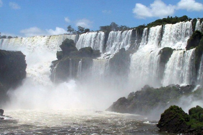A multi-tiered waterfall with mist and water spray, surrounded by rocky terrain and greenery. 2