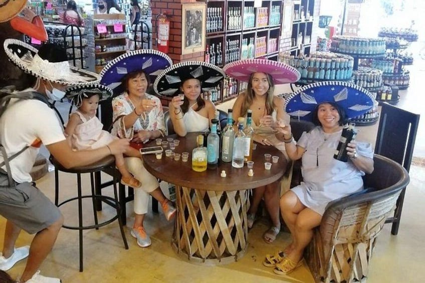 Un grupo de personas sentadas alrededor de una mesa con bebidas, usando sombreros, en una tienda con estantes llenos de botellas. 4