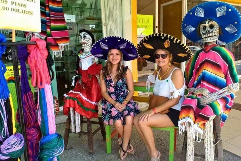 Two people sitting on chairs, one wearing a colorful dress and a large sombrero, and the other in a white top and black skirt. 3