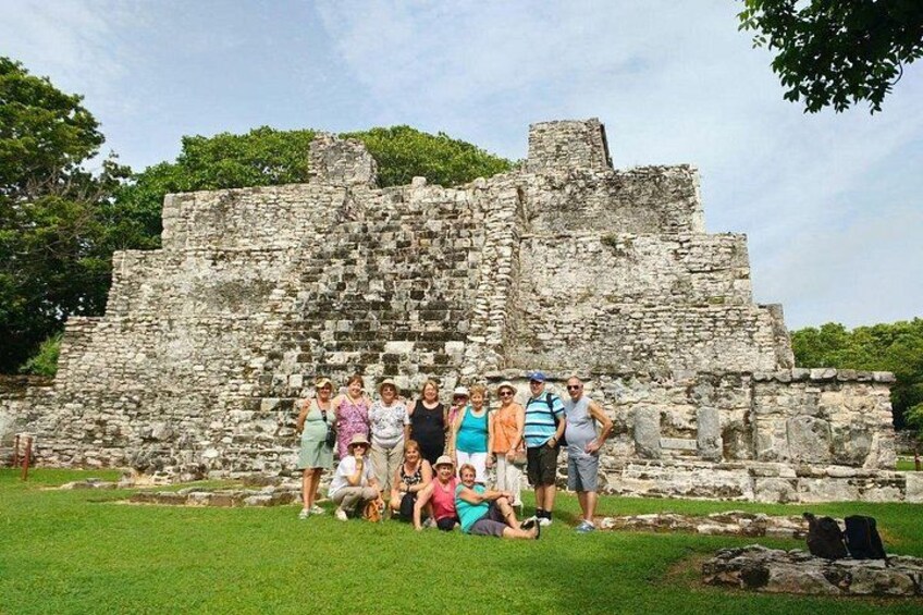 A group of people posing in front of ancient ruins with a grassy foreground and trees in the background. 2