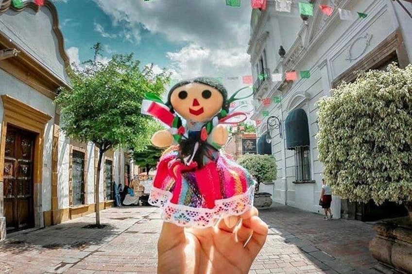Traditional Mexican doll and the beautiful regional architecture in the background. You can buy these souvenirs and more in Tonala and Tlaquepaque. 2