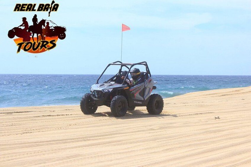 A beach with a dune buggy parked on the sand near the water. 2
