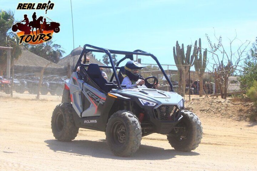 A Polaris off-road vehicle on a dirt road with cacti and a clear sky in the background. 2