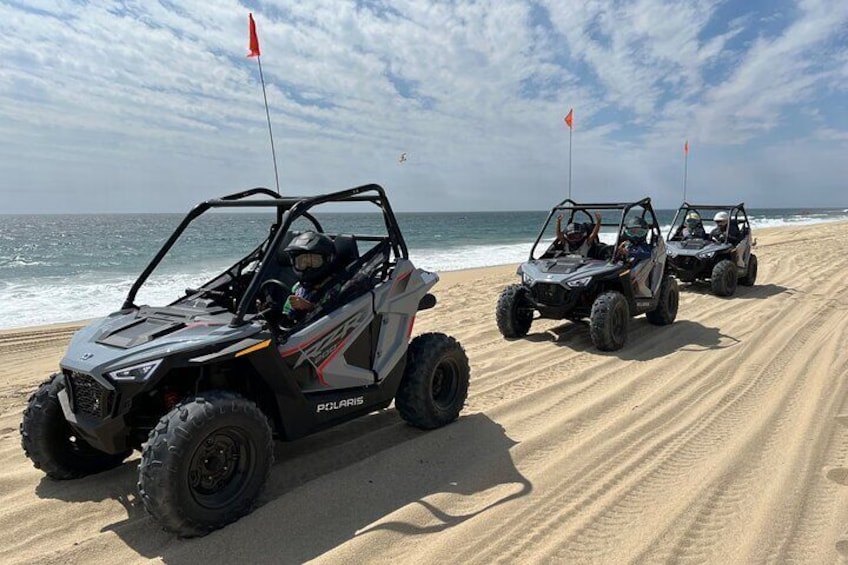 Three Polaris ATVs parked on a sandy beach with the ocean in the background. 1