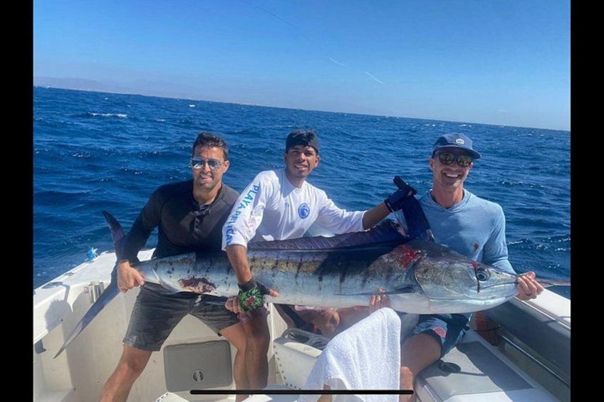 Three people on a boat holding a large fish. 3