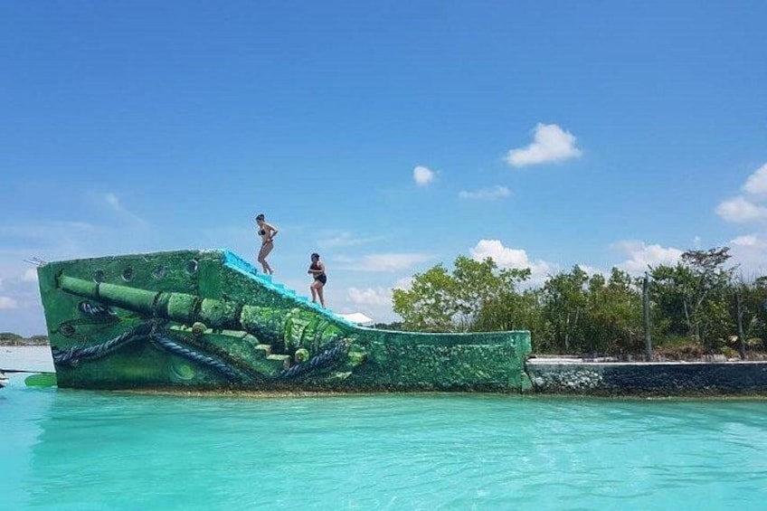 A green submarine-like structure in a clear blue pool with two people standing on it. 2