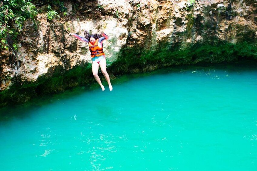 A person jumping into a turquoise pool with rocky cliffs in the background. 3