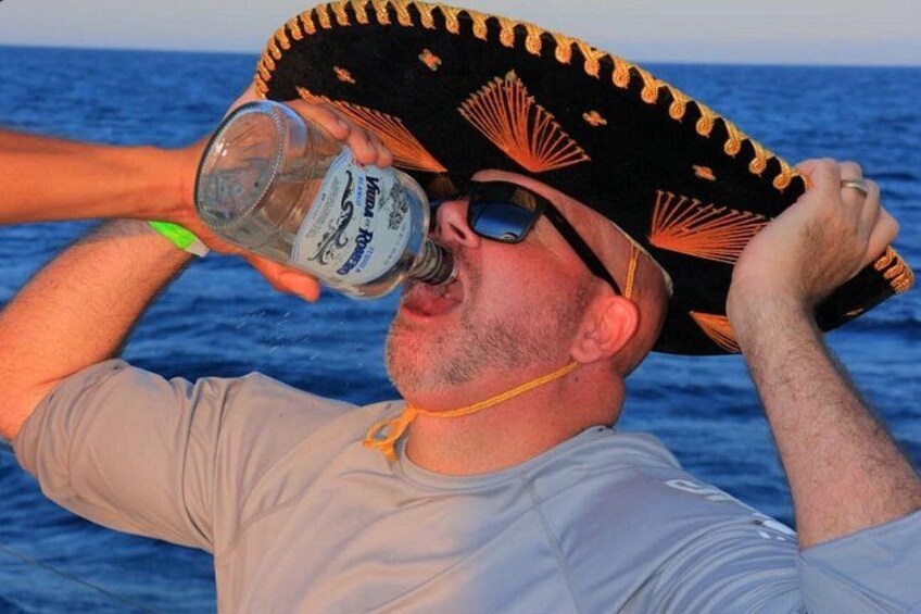 A person wearing a sombrero, holding a bottle, and standing by the sea. 4