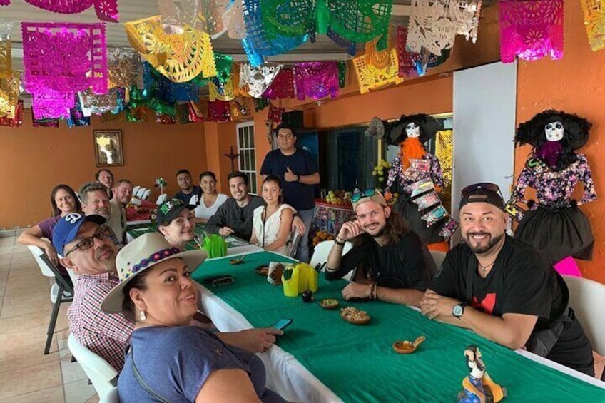 Un grupo de personas sentadas alrededor de una mesa con mantel verde, decorada con artesanías de papel y muñecas coloridas. 3
