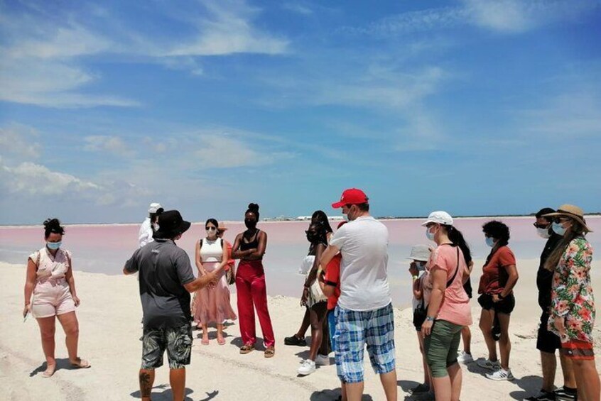 A group of people standing on a beach with a pinkish water body in the background. 5