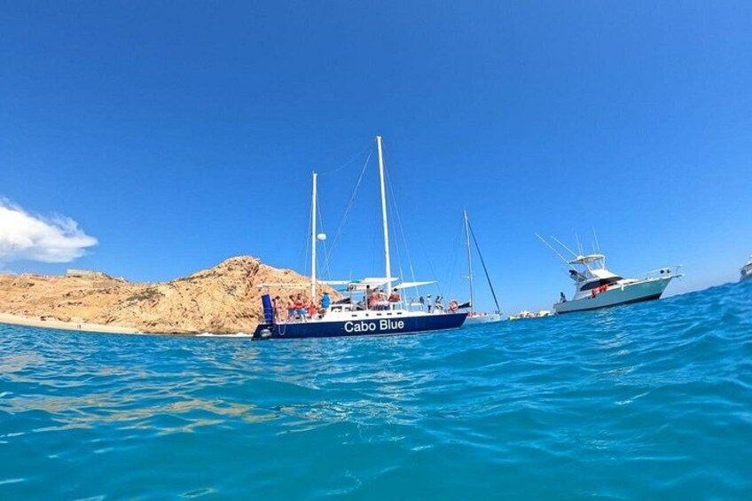 Un barco azul llamado Cabo Blue en aguas azules tranquilas, con una costa rocosa al fondo. 1