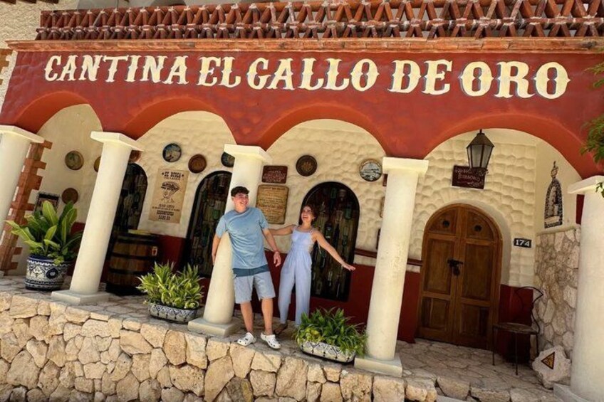 A building with the sign 'CANTINA EL CALLO DE ORO' and a stone wall with potted plants. 4
