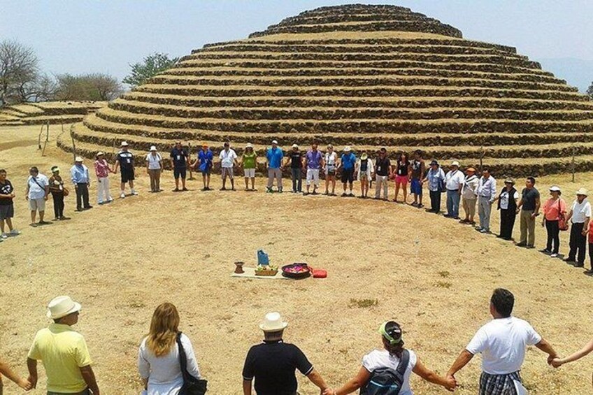 A group of people standing in a circle around a large, tiered structure in a desert landscape. 1