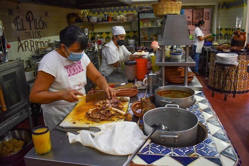 A bustling kitchen with chefs preparing food, a tiled backsplash, and a sign reading 'El Pilón de los Arribados'. 4