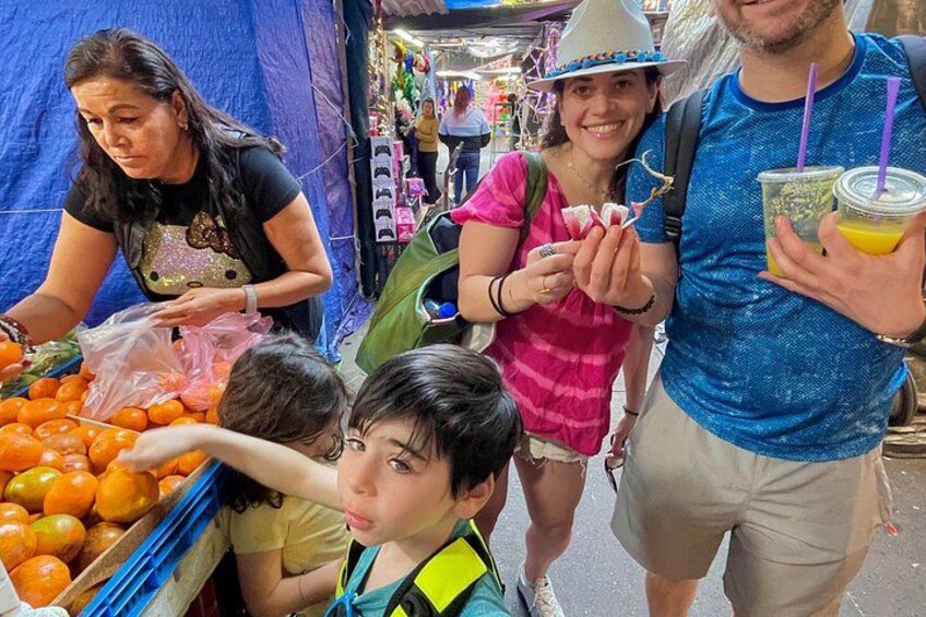 Escena de mercado con gente comprando y un niño alcanzando naranjas. 5