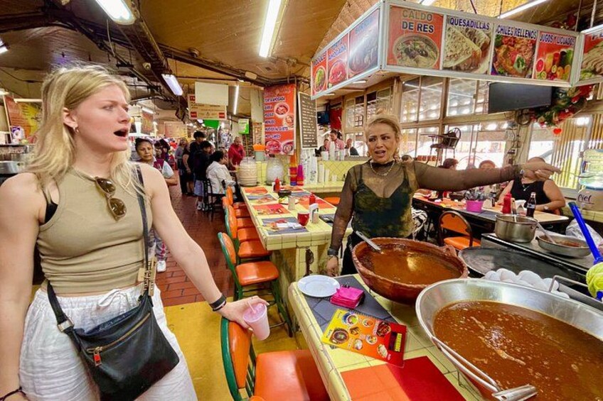 Una persona señala un puesto de comida en un mercado concurrido, donde se exhiben diversos productos alimenticios. 4