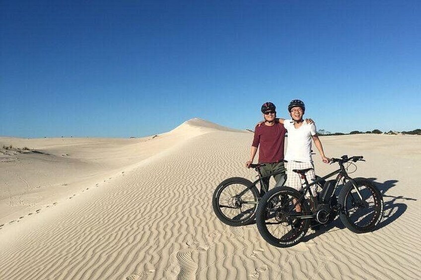 Two people standing on a sand dune with bicycles. 4
