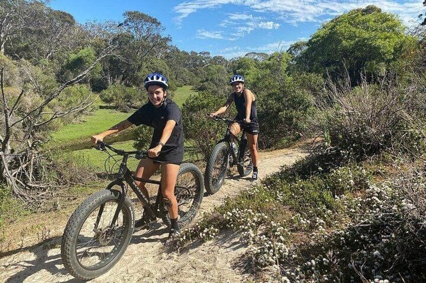 Two cyclists on a dirt path surrounded by greenery. 2
